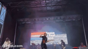 A Group Of People Are Playing Instruments On A Stage With A Large Screen Behind Them That Says ' Sheep Hop Band ' GIF