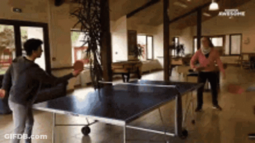 A Group Of People Are Playing Ping Pong In A Room GIF
