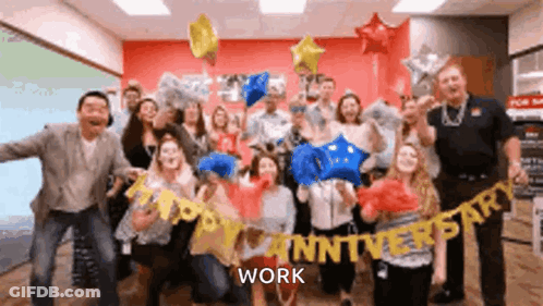 A Group Of People Are Posing For A Picture With Balloons And A Banner That Says Happy Anniversary Work . GIF