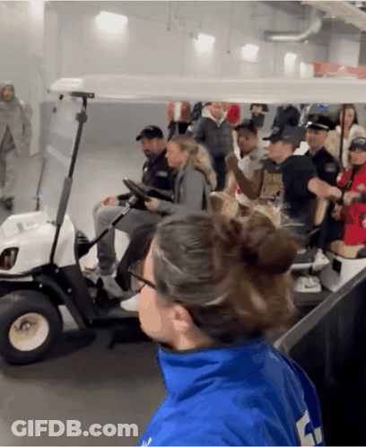 A Group Of People Are Riding In A Golf Cart And One Of Them Is Wearing A Blue Jacket With The Number 4 On It GIF