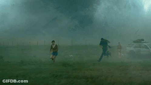 A Group Of People Are Running From A Tornado In A Field GIF