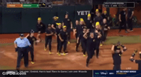 A Group Of People Are Running On A Baseball Field With A Scoreboard In The Background GIF