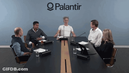A Group Of People Are Sitting Around A Conference Table With A Palantir Logo Behind Them GIF