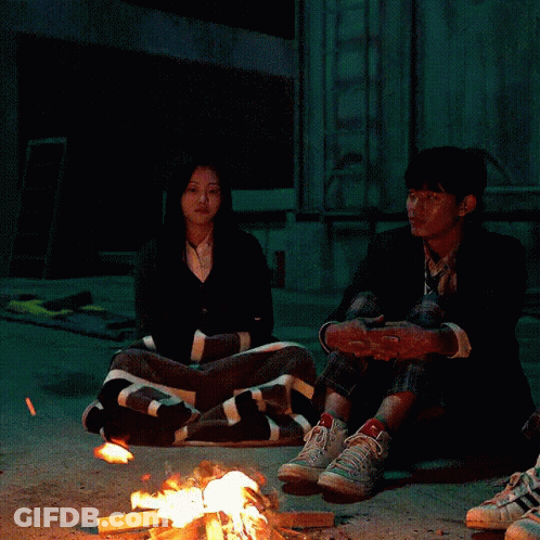 A Group Of People Are Sitting Around A Fire GIF
