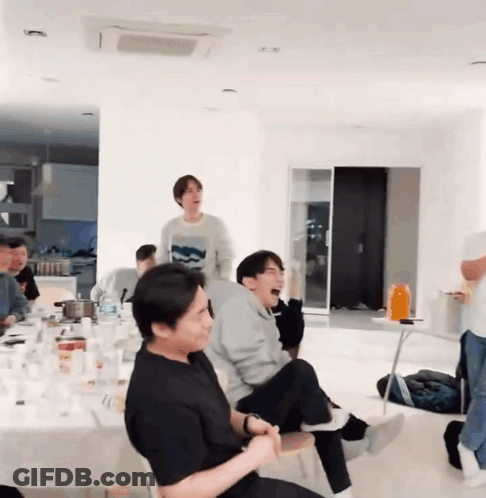 A Group Of People Are Sitting Around A Table In A Living Room . GIF