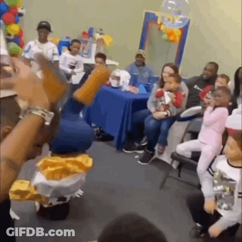 A Group Of People Are Sitting Around A Table In A Room With Balloons . GIF