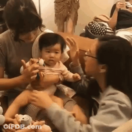 A Group Of People Are Sitting Around A Table With A Baby In Their Lap . GIF