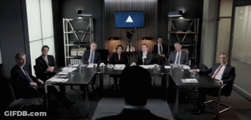 A Group Of People Are Sitting Around A Table With A Large Screen Behind Them That Says ' Triangle ' GIF