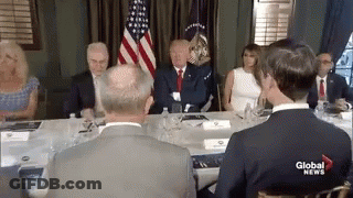 A Group Of People Are Sitting Around A Table With A Man In A Suit . GIF