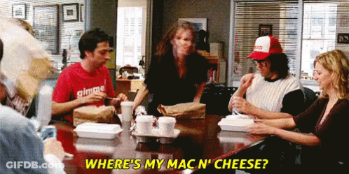 A Group Of People Are Sitting Around A Table With A Man Wearing A Red Shirt That Says Gimme GIF