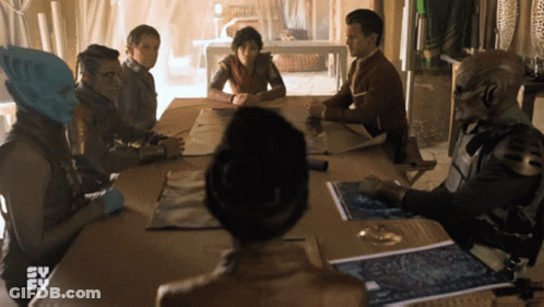 A Group Of People Are Sitting Around A Table With A Tv Logo In The Background GIF