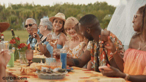 A Group Of People Are Sitting Around A Table With Glasses Of Wine GIF