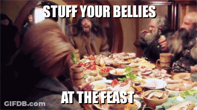 A Group Of People Are Sitting Around A Table With Plates Of Food And A Caption That Says Stuff Your Bellies At The Feast GIF
