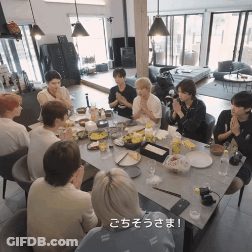 A Group Of People Are Sitting Around A Table With Plates Of Food And A Sign That Says " ごちそうさま " GIF