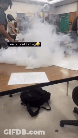 A Group Of People Are Sitting Around A Table With Smoke Coming Out Of It And A Sign That Says We R Retiring GIF