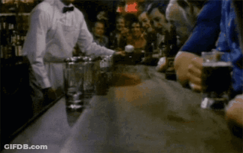 A Group Of People Are Sitting At A Bar With A Man In A Bow Tie Behind Them GIF