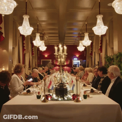 A Group Of People Are Sitting At A Long Table In A Room With A Sign That Says Ls Chamber Film Festival GIF