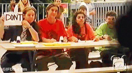 A Group Of People Are Sitting At A Table Holding A Sign That Says `` Don 'T '' . GIF