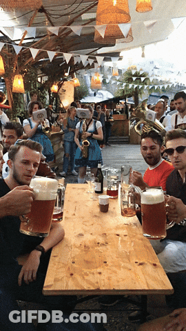 A Group Of People Are Sitting At A Table Holding Mugs Of Beer GIF