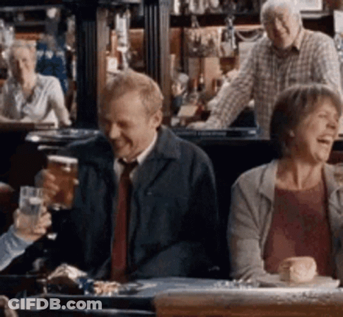 A Group Of People Are Sitting At A Table In A Bar Drinking Beer And Laughing . GIF