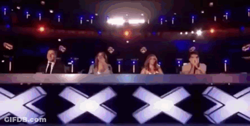 People Sitting At Table In Front Of Stage With X Sign GIF
