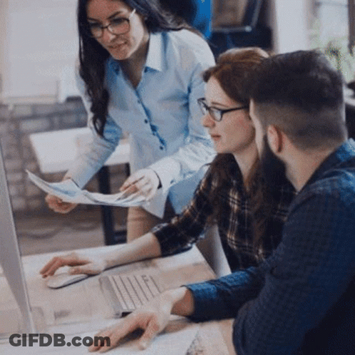 A Group Of People Are Sitting At A Table Looking At A Laptop Computer . GIF