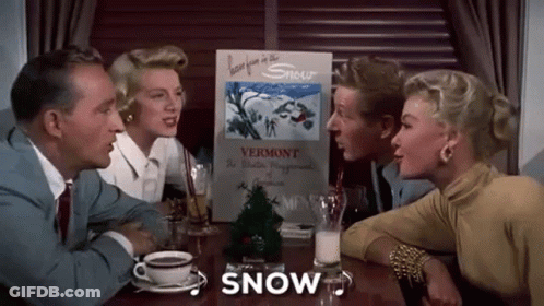 A Group Of People Are Sitting At A Table With A Sign That Says `` Snow '' . GIF