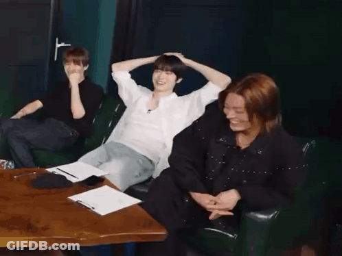 A Group Of People Are Sitting At A Table With Their Arms Over Their Head . GIF