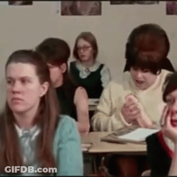 A Group Of People Are Sitting At Desks In A Classroom With Posters On The Wall GIF