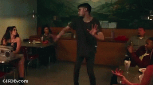A Group Of People Are Sitting At Tables In A Diner With A Man Standing In The Background . GIF