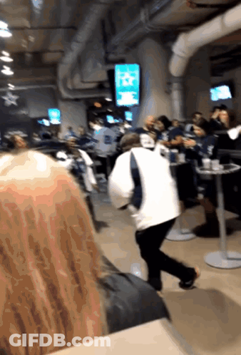 A Group Of People Are Sitting At Tables In A Room With A TV Screen That Says ' NFL ' On It GIF