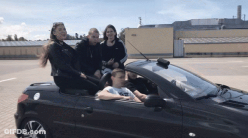 A Group Of People Are Sitting In A Convertible Car With A Man Driving GIF