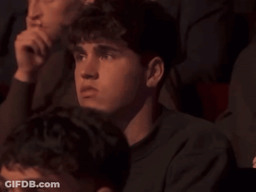 A Group Of People Are Sitting In A Dark Room And One Of Them Is Looking At Something GIF
