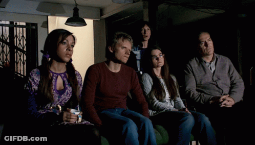 A Group Of People Are Sitting In A Dark Room And One Woman Is Holding A Cup Of Coffee GIF