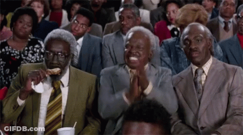 A Group Of People Are Sitting In A Room And One Man Is Eating A Piece Of Food GIF