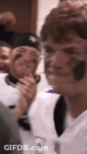 A Group Of People Are Sitting In A Room And One Of Them Is Wearing A Baseball Helmet On His Face . GIF