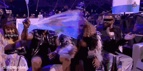 A Group Of People Are Sitting In A Stadium Holding Flags And One Of Them Is Wearing Sunglasses GIF