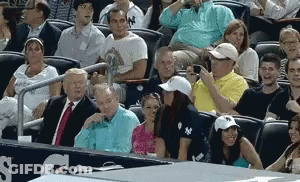 A Group Of People Are Sitting In A Stadium Watching A Baseball Game And One Of Them Is Wearing A Ny Hat GIF