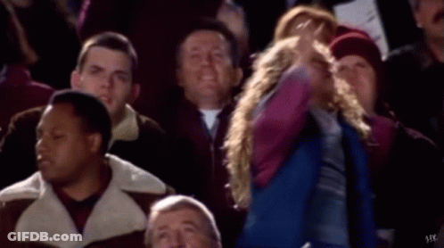 A Group Of People Are Sitting In A Stadium Watching A Game And A Girl Is Standing In The Middle Of The Audience . GIF