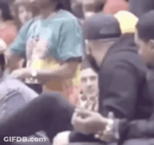 A Group Of People Are Sitting In A Stadium Watching A Game And One Of Them Is Using A Cell Phone . GIF