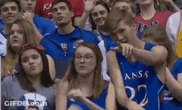 A Group Of People Are Sitting In A Stadium Wearing Kansas Shirts GIF