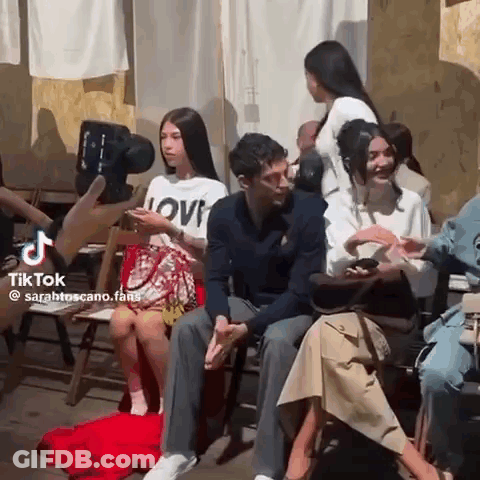 A Group Of People Are Sitting In Chairs Talking To Each Other While A Cameraman Takes A Picture Of Them . GIF