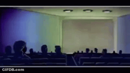 A Group Of People Are Sitting In Front Of A Screen In A Room GIF