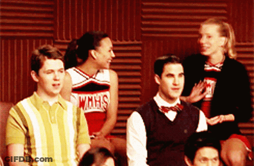 A Group Of People Are Sitting In Front Of A Wall And One Of The Cheerleaders Is Wearing A Wmhs Shirt GIF