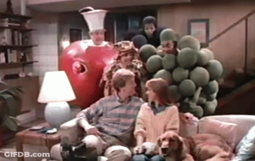 A Group Of People Are Sitting On A Couch In A Living Room With A Giant Apple Behind Them . GIF