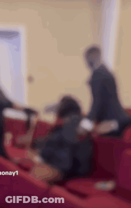 A Group Of People Are Sitting On Red Couches In A Room . GIF