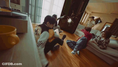 A Group Of People Are Sitting On The Floor In A Living Room And One Of Them Has The Word Adidas On His Back GIF