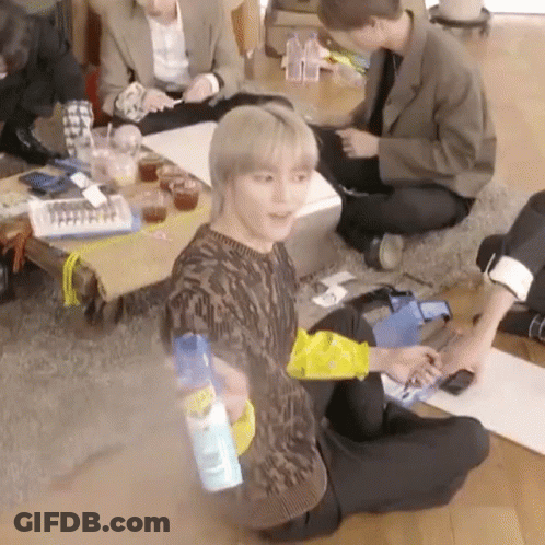 A Group Of People Are Sitting On The Floor In A Living Room . One Of The Men Is Holding A Spray Bottle . GIF