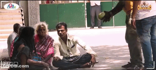 A Group Of People Are Sitting On The Ground And A Man Is Giving A Bottle Of Water GIF