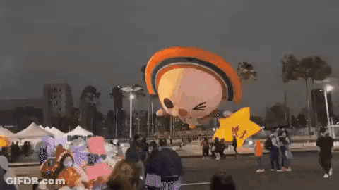 A Group Of People Are Standing Around A Balloon That Looks Like A Cat Flying In The Air . GIF